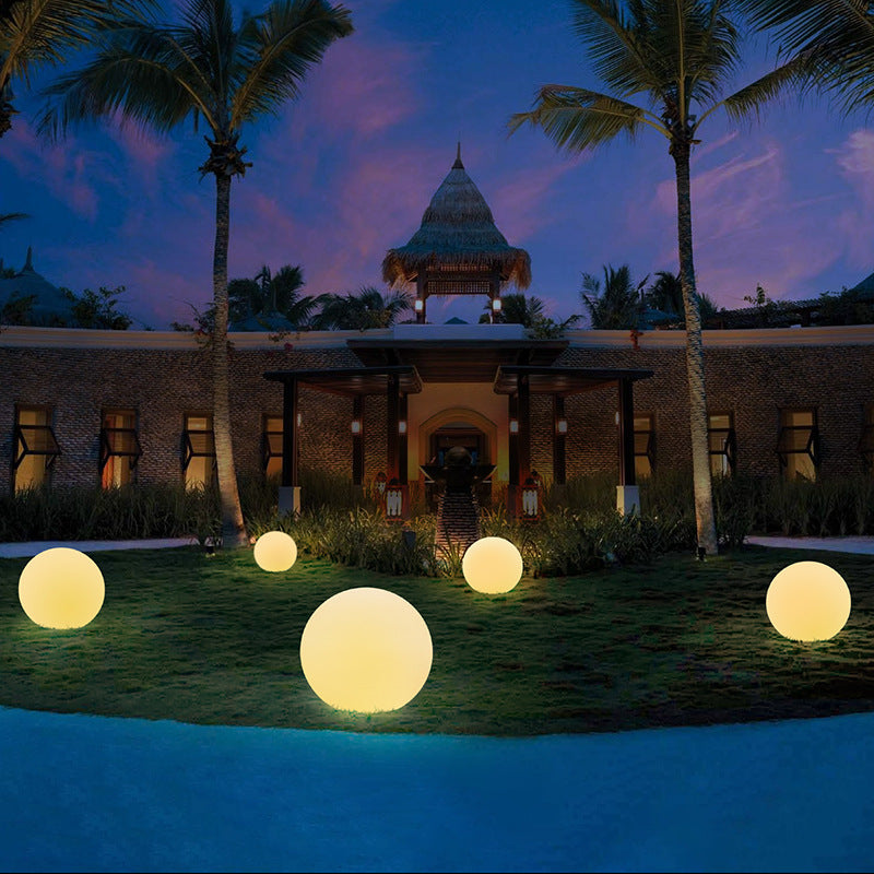 Glowing spherical outdoor lights arranged on grass with a building and palm trees in the background.