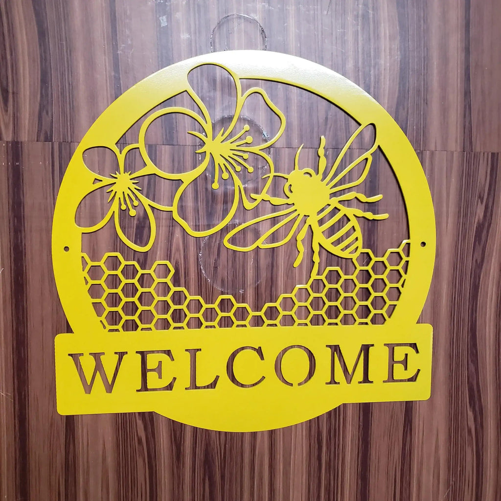 Yellow metal wall sign with a bee, flowers, honeycomb pattern, and the word 'WELCOME' in cutout letters, mounted against a dark wood-paneled wall.